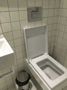 クオリティ ホテル グローブのバスルーム内トイレ設備。白いタイル張りの壁とシンプルな壁掛けトイレが特徴。