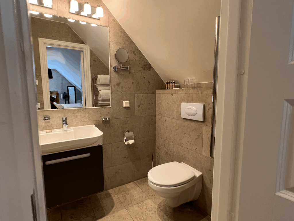 Hotell Slottsbackenのバスルーム。明るい照明と大きな鏡、清潔感のある洗面台とトイレが揃った機能的な空間。