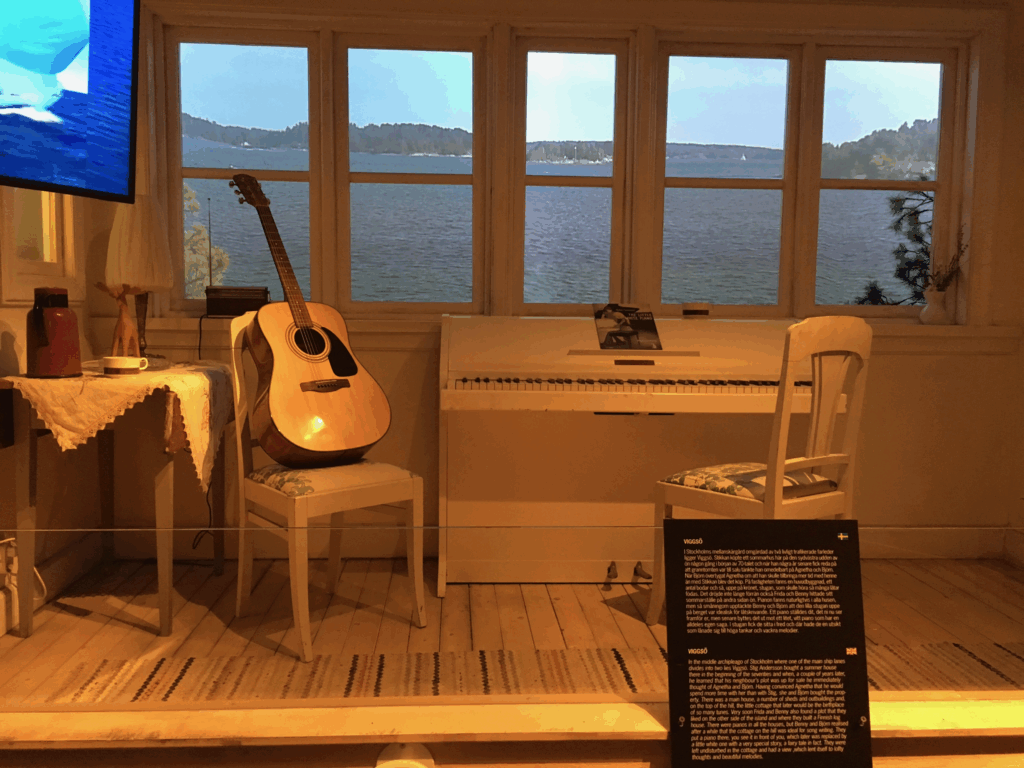 ギターと白いピアノが置かれた作曲風景を再現した展示。背景にはスウェーデンの美しい湖の映像