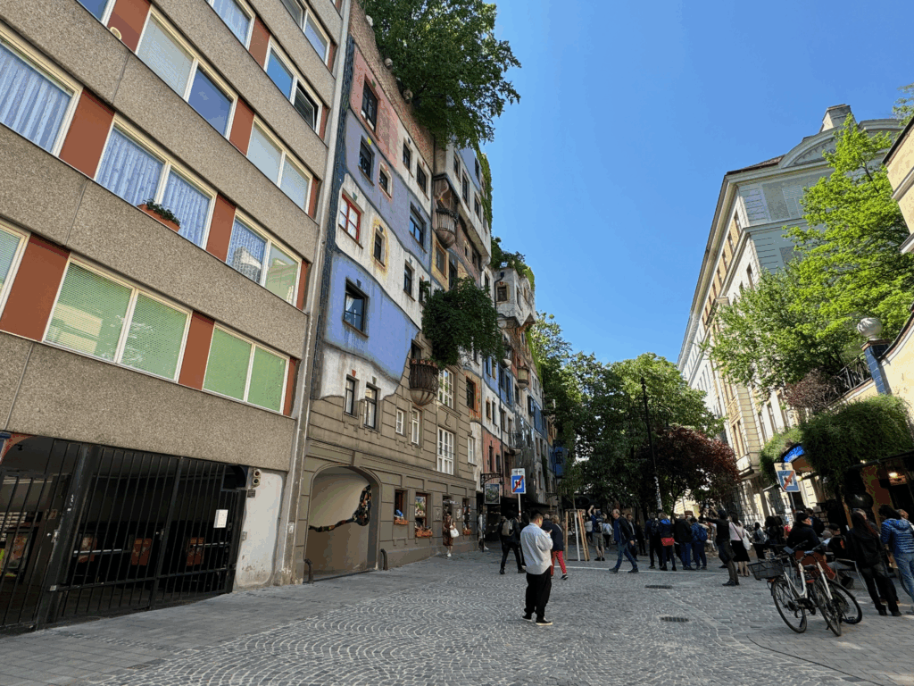 フンデルトヴァッサーハウスの全景を遠景から捉えた写真。カラフルな建物が街並みに溶け込み、観光客が通りに集まっている様子。