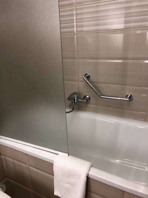 ガラス仕切りのある清潔なバスタブ。手すり付きで安全に配慮されたバスルーム設備