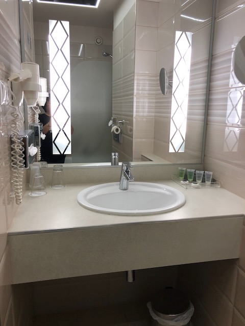 鏡の横にドライヤーが設置された洗面台。明るい照明と広めのシンク